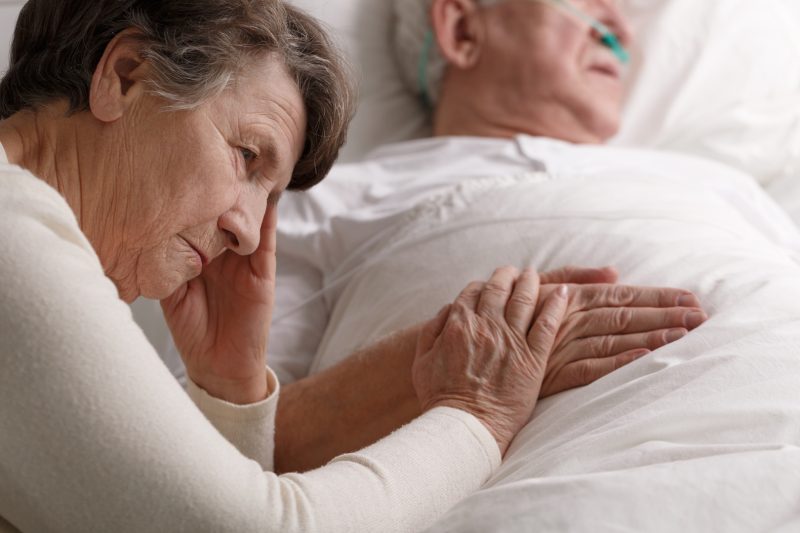 Besorgte Seniorin hält Hand ihres kranken Mannes