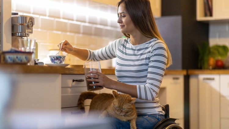 Junge Frau im Rollstuhl macht Kaffee in ihrer Küche