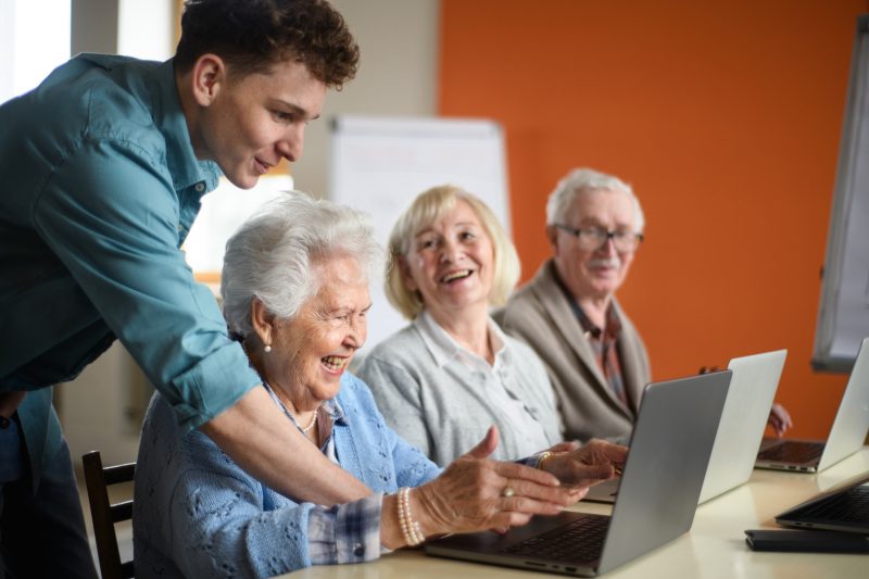 Junger Mann erklärte etwas am Computer älteren Menschen