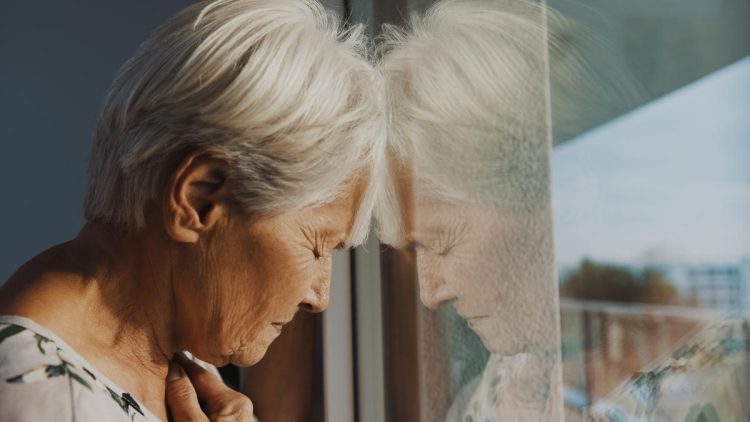 Einsamkeit durch Care-Arbeit - Frau mit geschlossenen Augen und Kopf an eine Fensterscheibe gelehnt