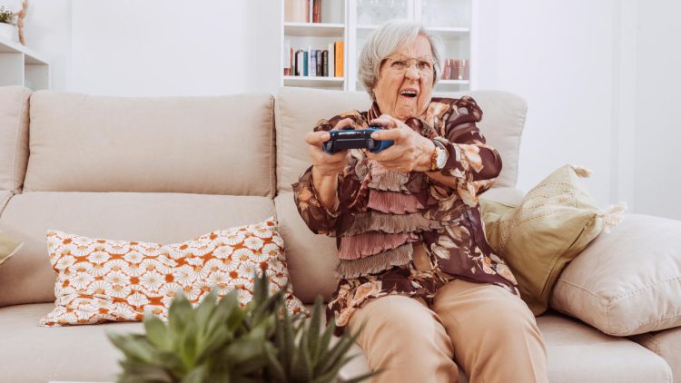 Ältere Dame mit Controller in der Hand beim Konsolenspiel auf der Couch